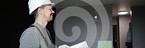 Young smiling repairman standing in empty flat and holding construction plan in hands