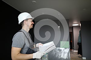 Young smiling repairman standing in empty flat and holding construction plan in hands