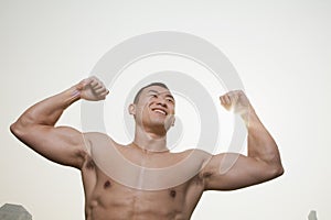 Young, smiling, shirtless young man flexing his muscles with arms raised outdoors in Beijing, China