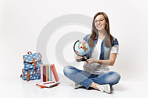 Young smiling smart woman student in glasses holding world globe learning geography sitting near backpack school book