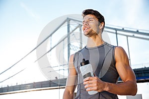 Young smiling sports man resting after running, holding water bottle