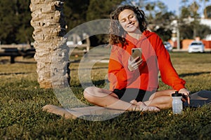 Young smiling sportswoman in wirelles headphones listening music and using cellphone during workout yoga practice photo