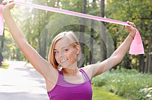 Young smiling sporty blonde woman training outdoor with resistance band