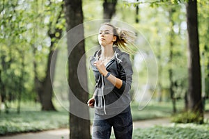 Young smiling sporty woman running in park in the morning. Fitness girl jogging in park