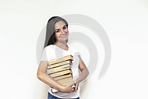 Young smiling student woman in white t-shirt holding textbooks and books in a pile on a white backdrop. College education concept