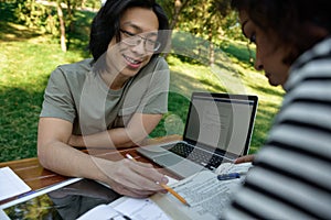 Young smiling students sitting and studying outdoors