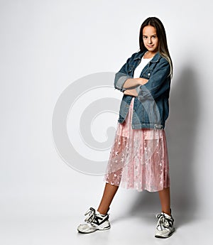 Young smiling teen girl in stylish casual clothes and sneakers standing and looking at camera over white background