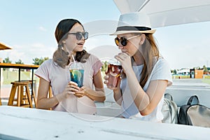 Young smiling teen girls drink cool refreshing summer drinks on a hot sunny day in summer outdoor cafe