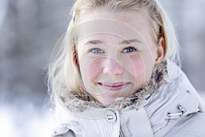 Young smiling teenage girl in a snowy park. Cute blonde in a white jacket. Walking in the fresh air in the winter and cold seasons