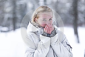 Young smiling teenage girl in a snowy park. Cute blonde in a white jacket. Walking in the fresh air in the winter and cold seasons