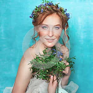 Young smiling tender woman with blue flowers on light blue background. Spring beauty portrait