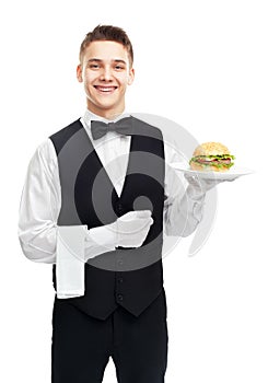 Young smiling waiter holding hamburger on plate