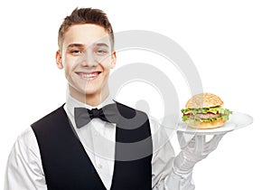 Young smiling waiter holding hamburger on plate