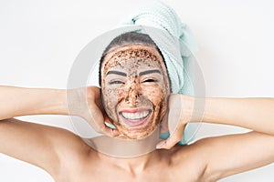 Young smiling woman applying coffee scrub mask on face - Happy girl having skin care spa day at home photo