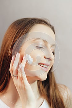 Young smiling woman is applying cream to her cheeks