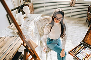 Young smiling woman artist, holding paintbrush and draws on canvas , working on a home art studio