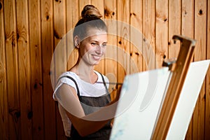 Young smiling woman artist paints on canvas at the easel