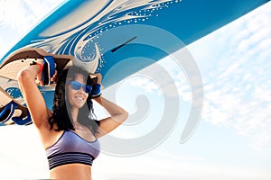 Young smiling woman on the beach carries a surfboard on her head