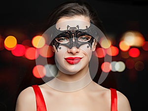 Young smiling woman in carnival mask on abstract red night glitter bokeh background