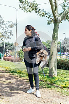 Young smiling woman carrying her dog in a backpack while talking on the phone, outdoor in nature.
