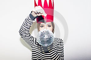 Young smiling woman celebrating party, wearing stripped dress and red paper crown, happy dynamic carnival disco ball