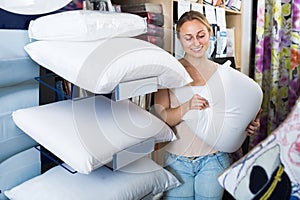 Young smiling woman choosing fluffy pillow