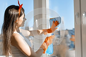 Young smiling woman cleaning window, with spray window cleaner and rag in rubber gloves, spring cleaning at home