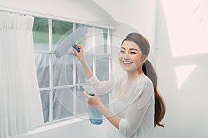 Young smiling woman is cleaning windows in a house, doing chores