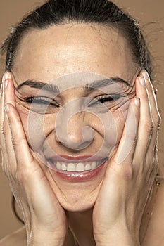 A young smiling woman crumples the skin of her face with her hands