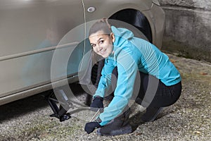 Young smiling woman driver changes car tyres