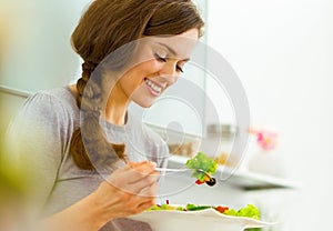 Young woman eating fresh salad in modern kitchen