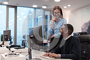 Young smiling woman explaining to serious African American coworker project strategy. Diverse startup coworkers students