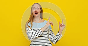 Young smiling woman with fair-haired gestures with hands, pointing fingers right, showing advertisement. Indoor studio shot on