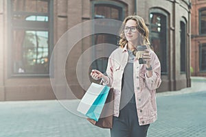 Young smiling woman in glasses carries shopping bags and holds cup of coffee.Girl bought presents for her friend.