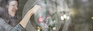 Young smiling woman hanging red holiday ball on a Christmas tree