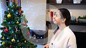 Young smiling woman hangs colorful balls on the Christmas tree