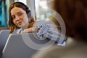 Young smiling woman in headphones listen music while traveling in public transport