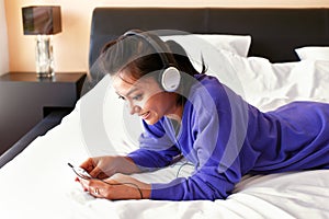 Young smiling woman in headphones listening to the music in bed