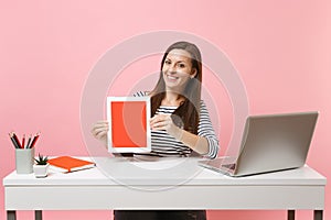 Young smiling woman hold tablet computer with blank empty screen sit work at white desk with contemporary pc laptop