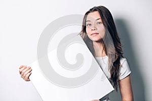Young smiling woman holding a blank sheet of paper for advertising.