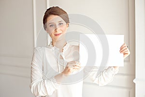 Young smiling woman holding a blank sheet of paper for advertising.Girl showing banner with copy space