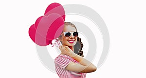 Young smiling woman holding bunch of pink heart shaped balloons on a white background