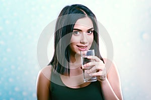 Young smiling woman holding and drinking water glass