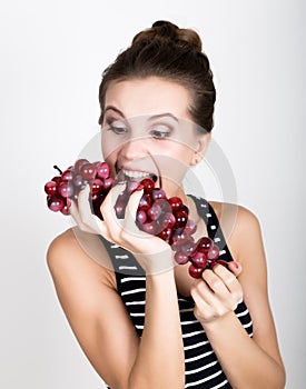 Young smiling woman holding fresh red bunch of grapes.