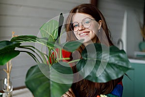 Young smiling woman holding home plant in a pot, comfort in the house and a tie behind the flowers