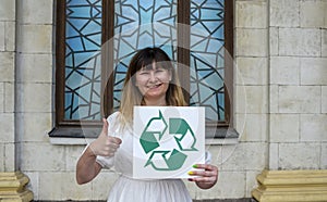 Young smiling woman holding placard with green recycling sign and showing thumb up