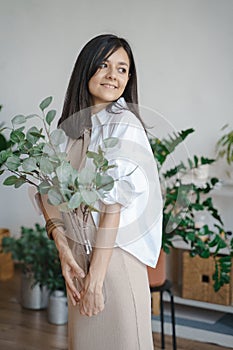 Young smiling woman holding a vase with eucalyptus branches at home. Naturalness and ecology concept