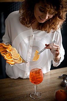 Young smiling woman holds metal tray with orange slices and decorates glass with drink