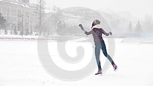 A young smiling woman ice skating outside. Heavy snowfall