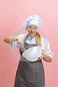 Young smiling woman, lady-cook, chef in white uniform cooking isolated on pink background. Cuisine, profession, business